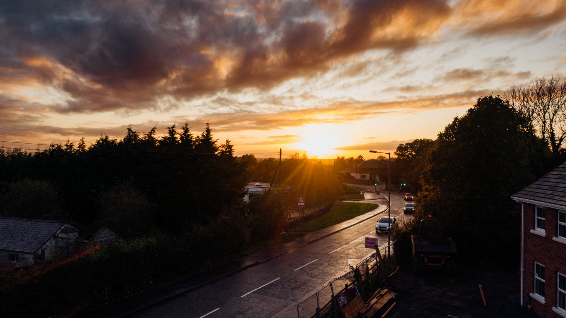 Scenic sunset view over a quiet urban street surrounded by trees and buildings, casting warm hues.