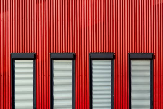 Red corrugated metal wall with four rectangular windows, capturing industrial design.