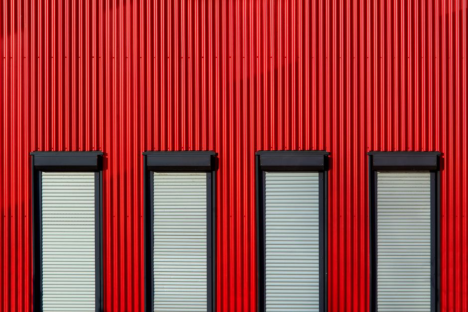 Red corrugated metal wall with four rectangular windows, capturing industrial design.