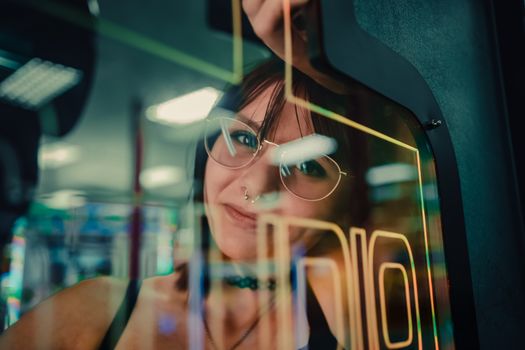 A woman reflected in arcade machine glass, enveloped in neon lights.