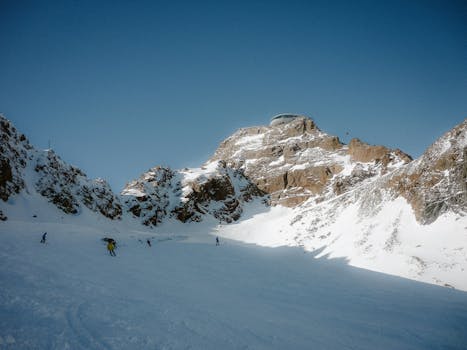 Skiers on a snowy mountain slope with a clear blue sky overhead.
