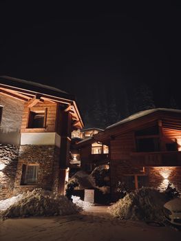 Charming wooden cabin illuminated at night, surrounded by snow in a serene winter setting.