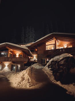 A wooden alpine chalet nestled in snowy mountains under the night sky.