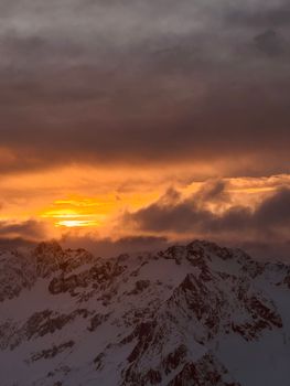 Breathtaking sunrise over snow-capped mountain range with dramatic clouds.