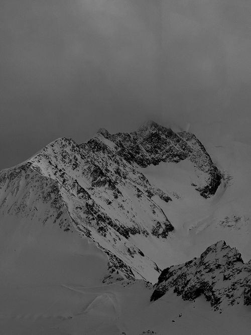 Free Black and white photograph of a rugged and snowy mountain peak under a cloudy sky. Stock Photo
