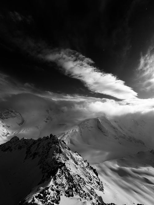 Free Atmospheric black and white photo of rugged snowy mountain peaks under a dramatic sky. Stock Photo