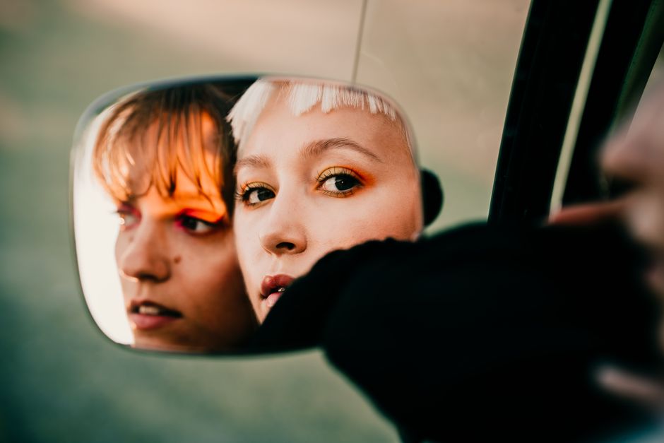 Stylish portrait of two women looking into a car mirror, capturing an intimate and artistic reflection.
