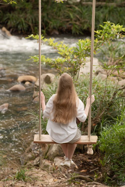 Free A girl on a swing overlooks a calm forest stream, embracing nature's serenity. Stock Photo