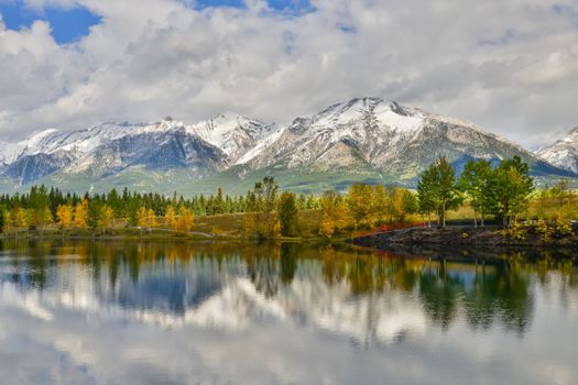 A serene autumn view of Canmore's snowy mountains reflecting in a calm lake.