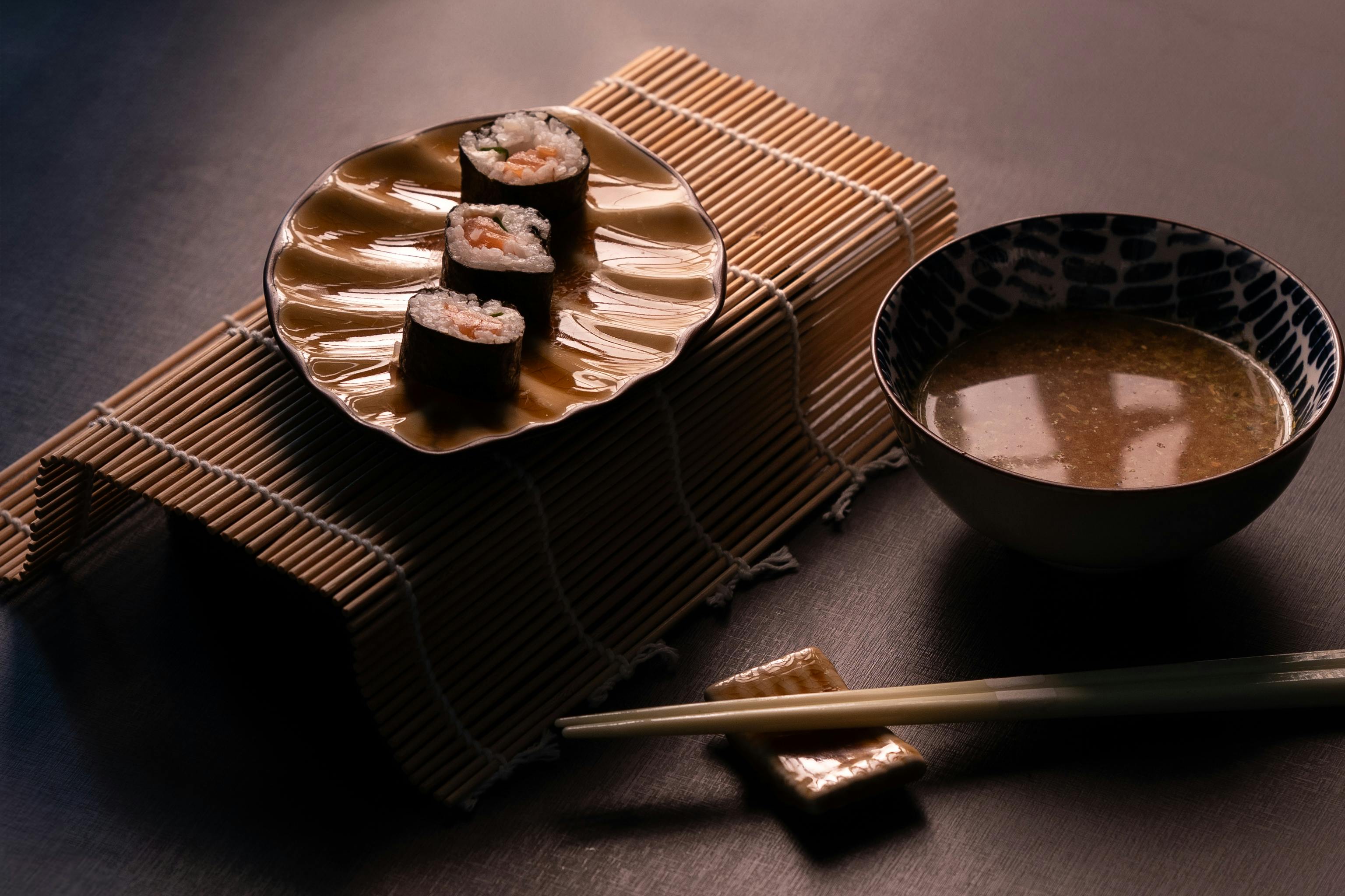 A serene presentation of sushi rolls and miso soup on a bamboo mat setting.