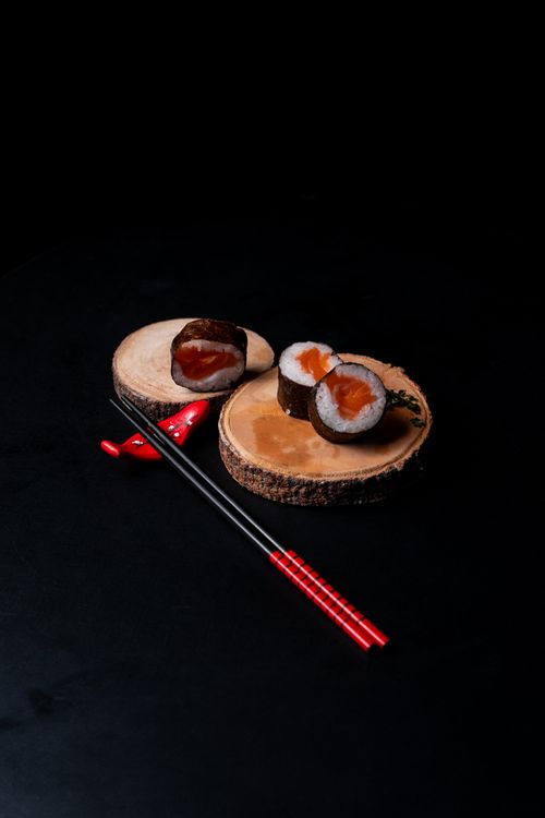 Free Elegant sushi rolls displayed on wooden slices, paired with traditional red chopsticks. Stock Photo
