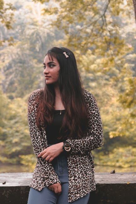 A young woman stands outdoors in casual attire, surrounded by greenery, embodying leisure and fashion.