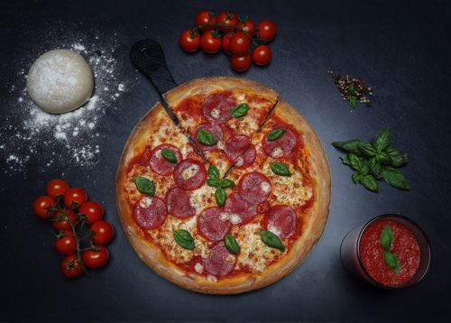 Free Top view of a pepperoni pizza surrounded by fresh ingredients including dough, tomatoes, and basil. Stock Photo