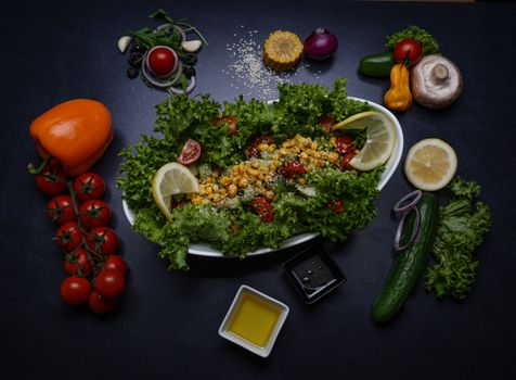 Healthy fresh salad surrounded by colorful vegetables and condiments on a dark background, perfect for food lovers.