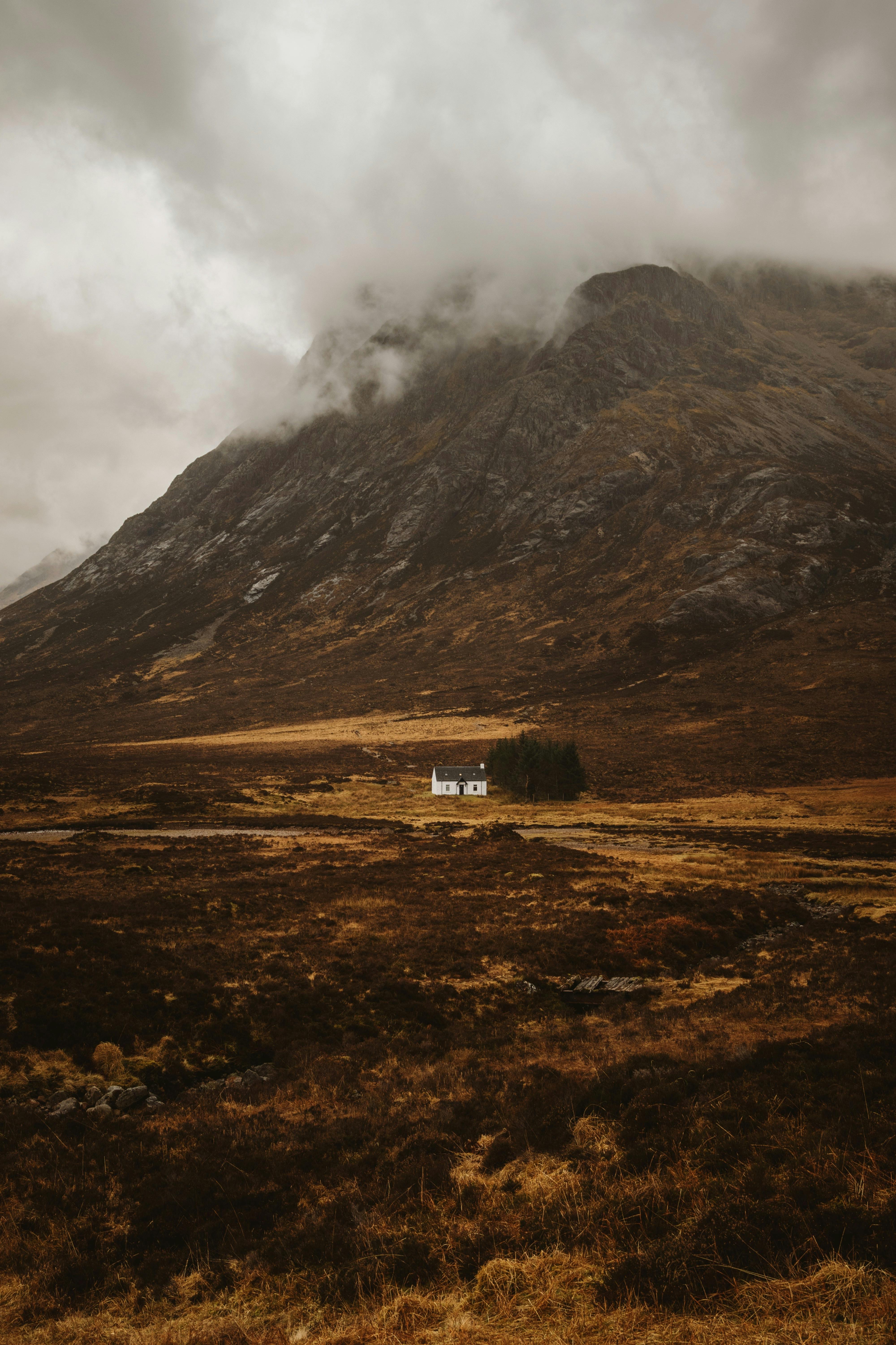 A solitary white house nestled in the dramatic landscape of Glencoe, Scotland, under a cloudy sky.