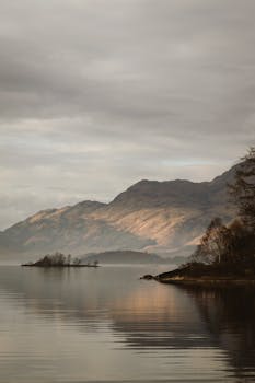 Misty morning view of Loch Lomond with mountains and calm waters in Scotland.