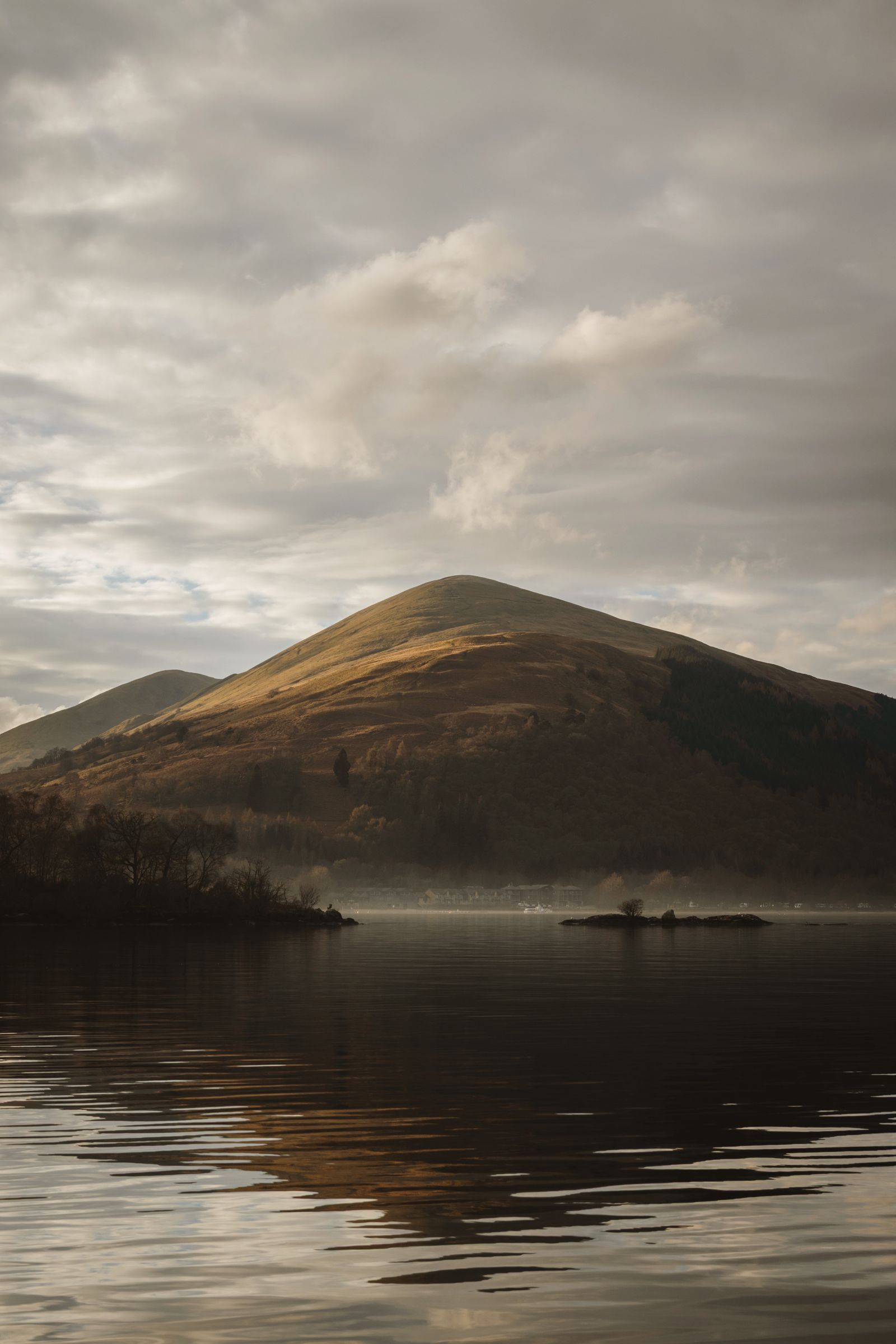 Misty morning view of Loch Lomond with mountains reflected in calm water, Scotland