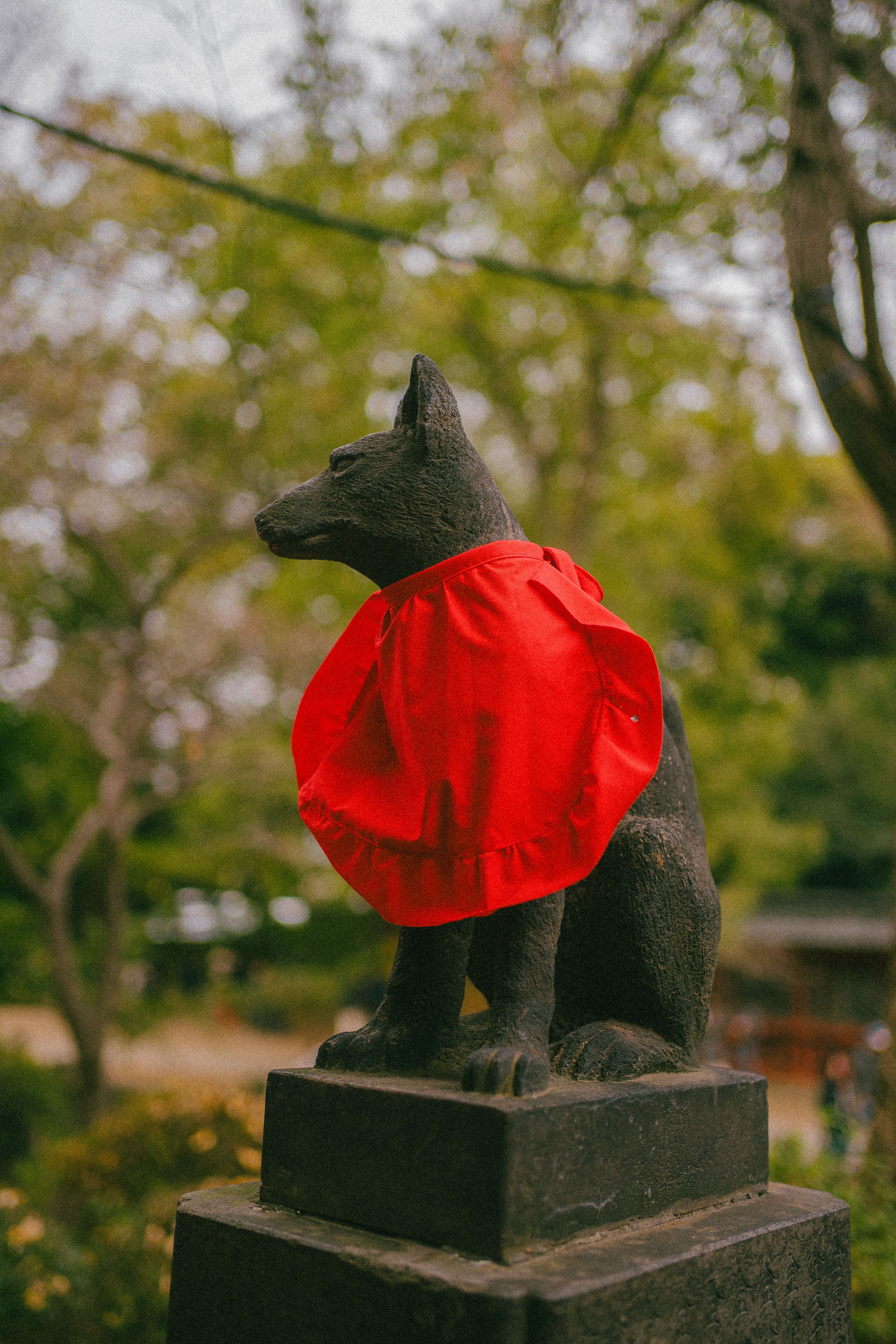 Statue of a fox wearing a red bib amidst lush outdoor greenery.