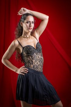 Stylish portrait of a woman in black lace dress with red backdrop, exuding confidence and elegance.