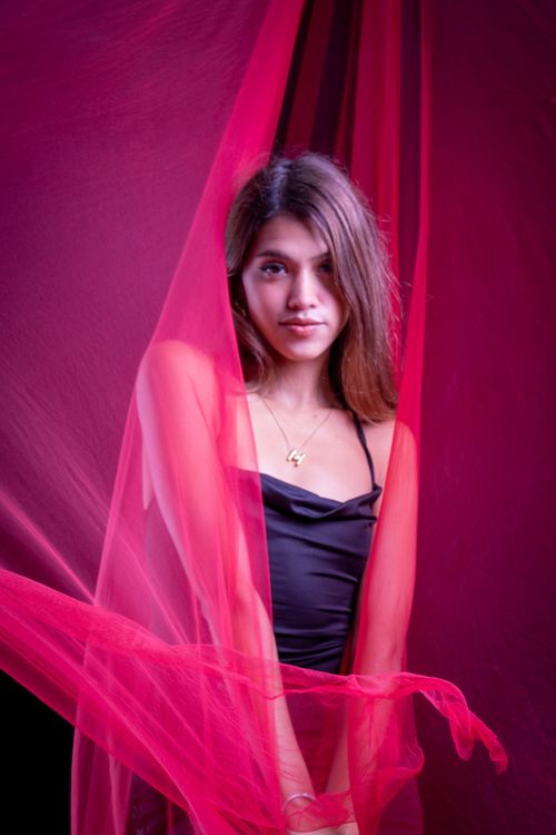 Free A young woman poses gracefully with red fabric, creating a vibrant and artistic portrait. Stock Photo