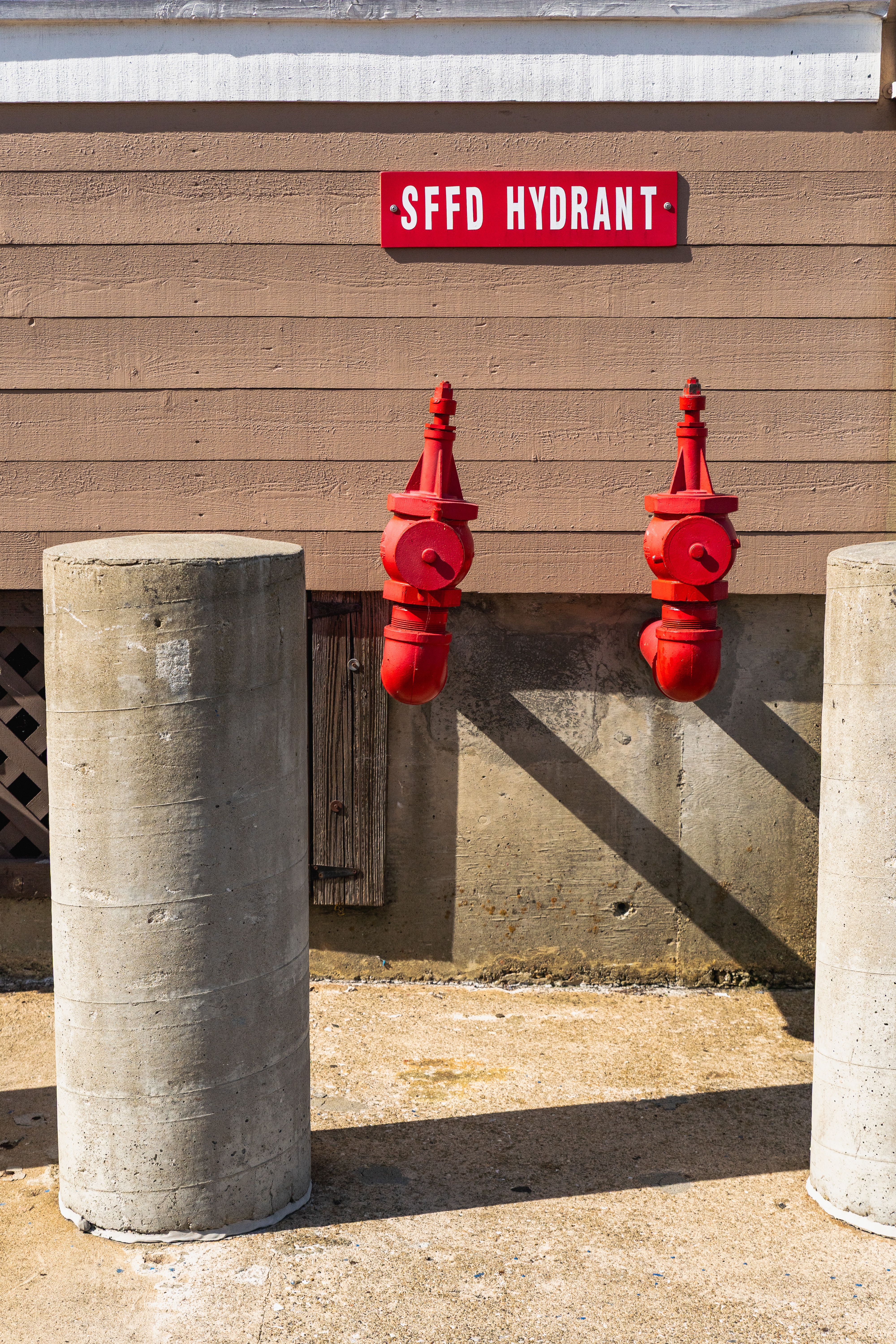 Bright red fire hydrants against a brown wall with distinct shadow play.