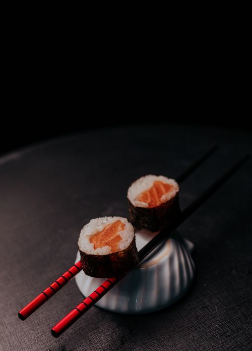 Free Close-up of sushi rolls with chopsticks on a dark background, emphasizing elegance and culinary artistry. Stock Photo