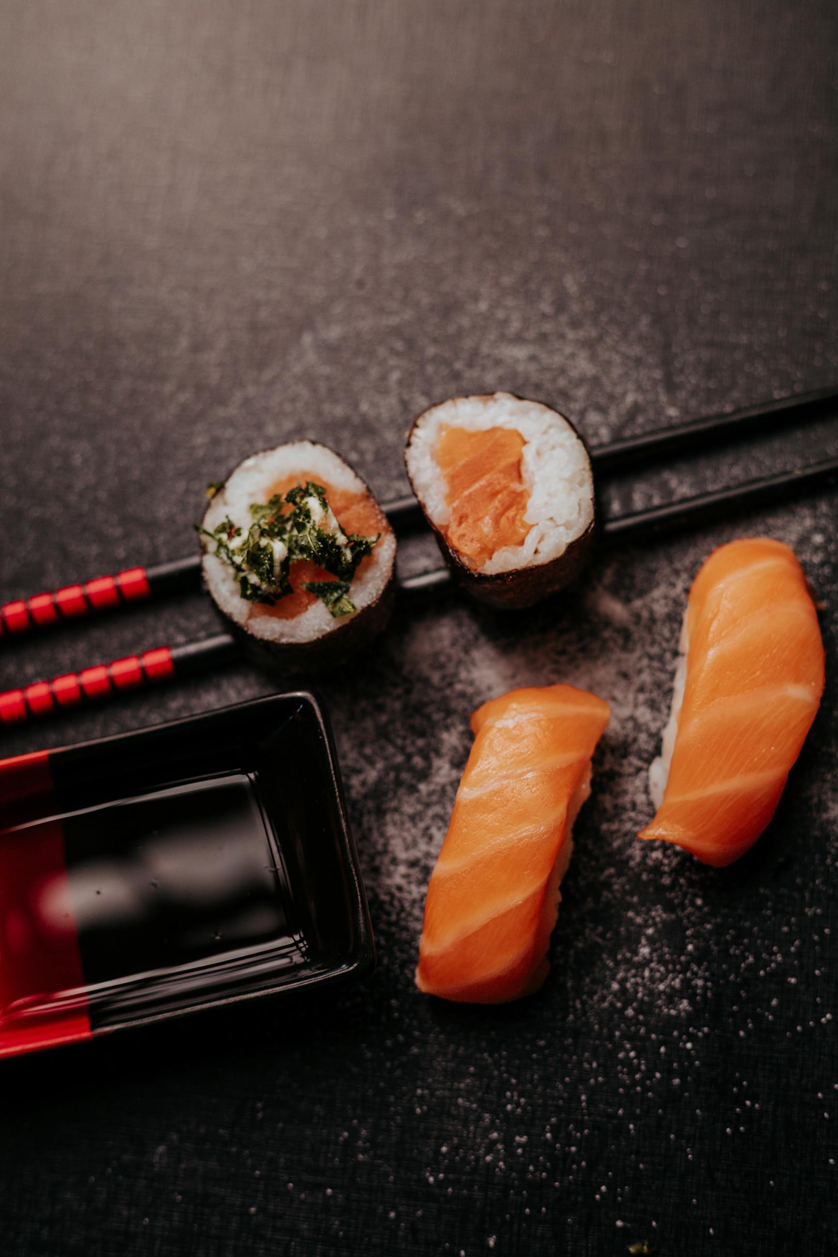 Close-up of sushi and sashimi with chopsticks on a dark table.