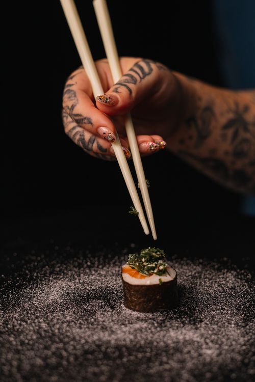Free Tattooed hand holding sushi with chopsticks on a dark background, dusted with seasoning. Stock Photo