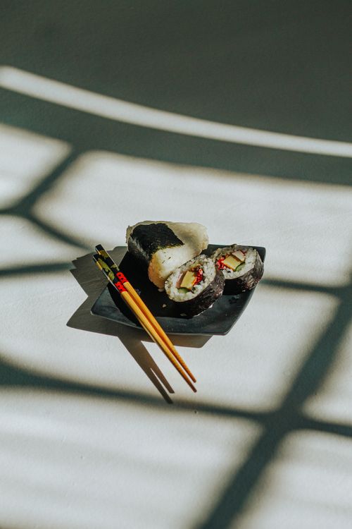 Free A square plate with sushi rolls and chopsticks, highlighted by dramatic shadows on a textured surface. Stock Photo