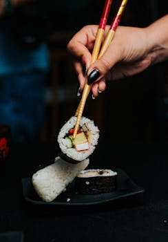 Close-up of a hand holding sushi roll with chopsticks, emphasizing Japanese culture and cuisine.