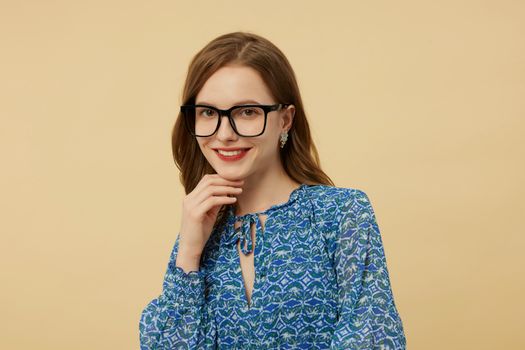 Portrait of a stylish woman wearing glasses and a blue patterned blouse against a beige background.