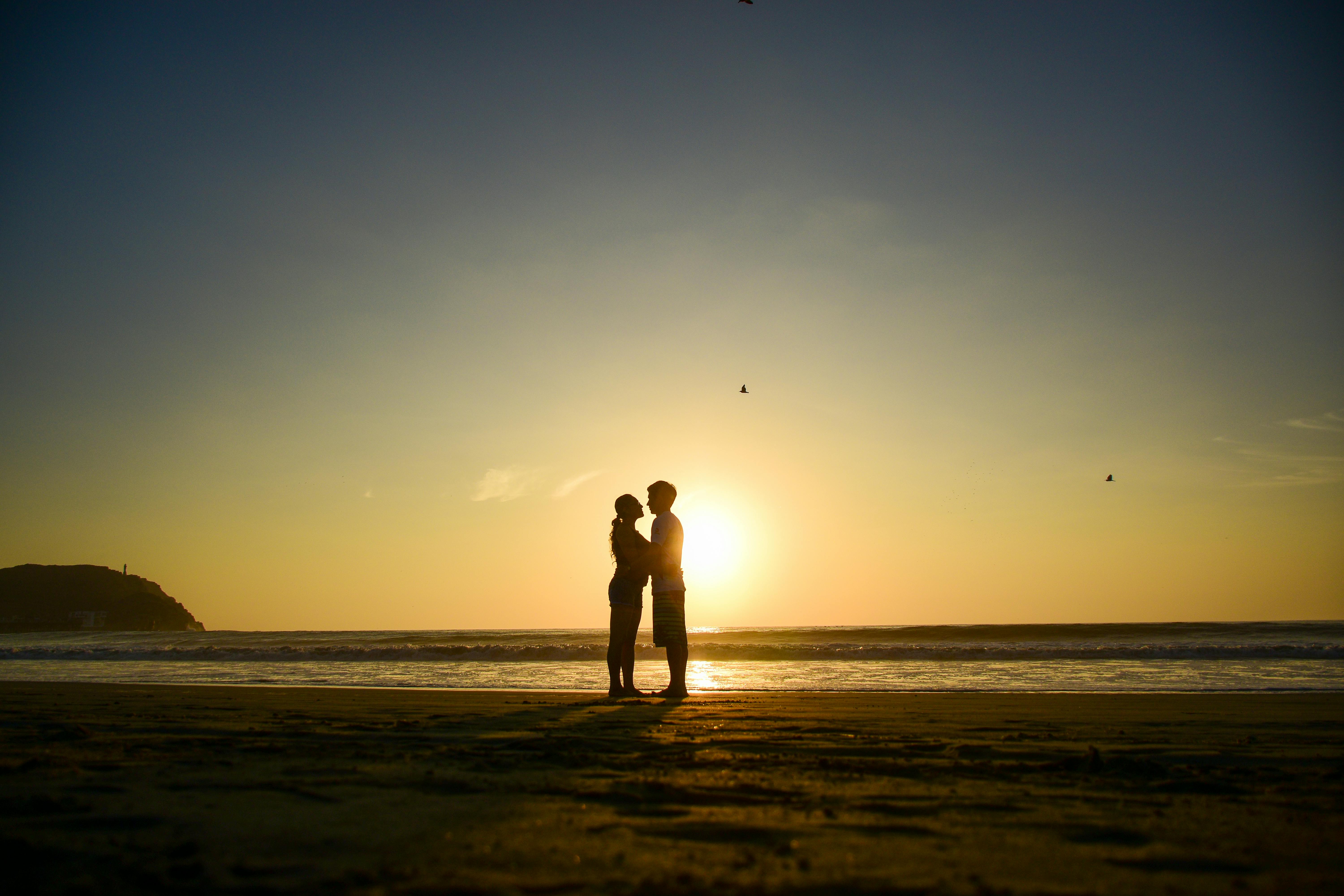 A romantic silhouette of a couple embracing on the beach during a vibrant sunset at Cerro Azul, Peru.
