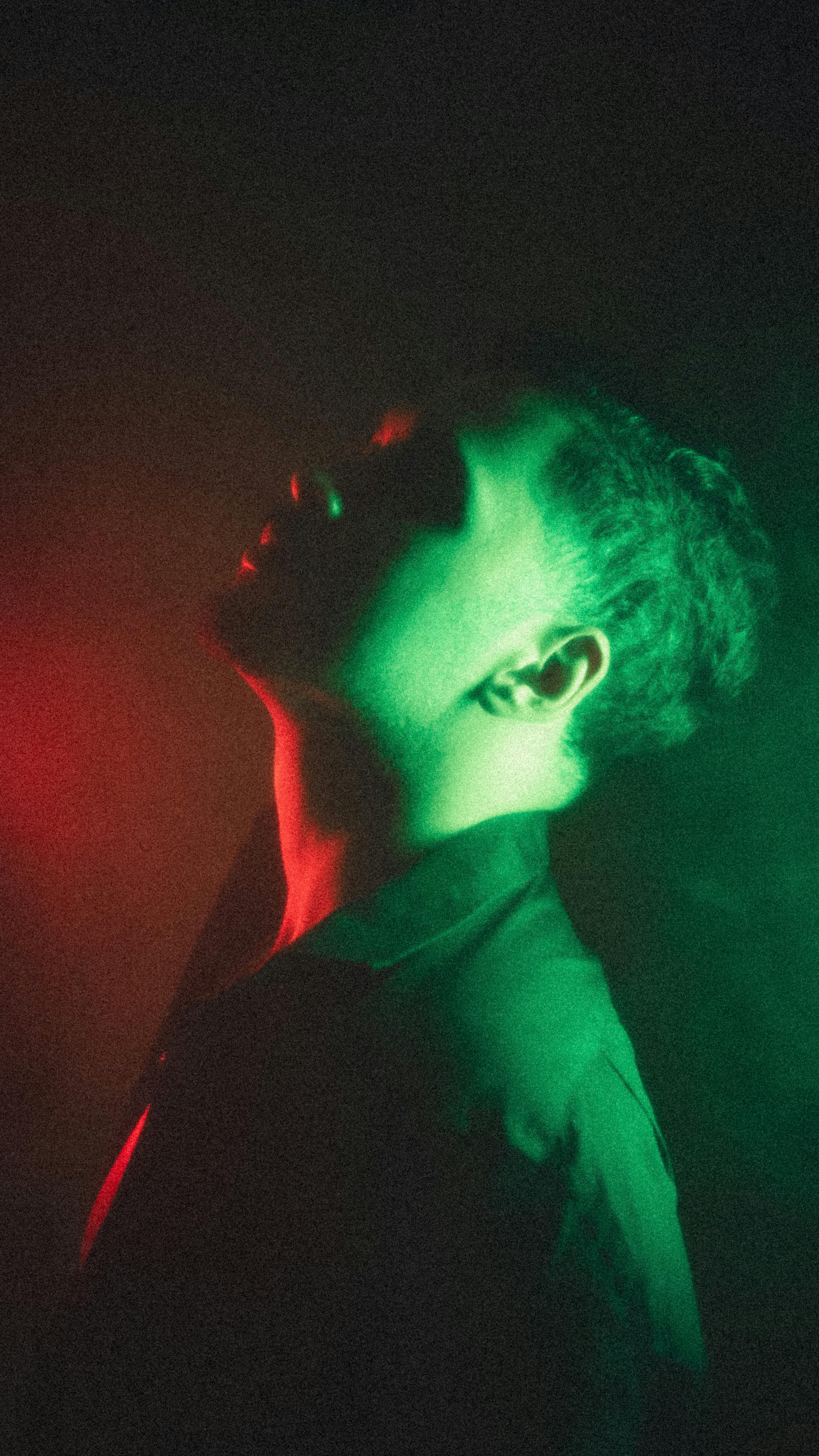 Artistic portrait of a man in profile, illuminated by vibrant red and green lighting, creating a dramatic atmosphere.