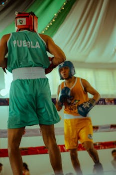 Two boxers intently facing off in a lively boxing match. Bright indoor setting with team uniforms.