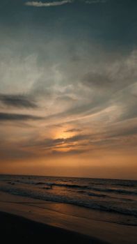 Capture of a serene beach at sunset with dramatic clouds and soft waves.