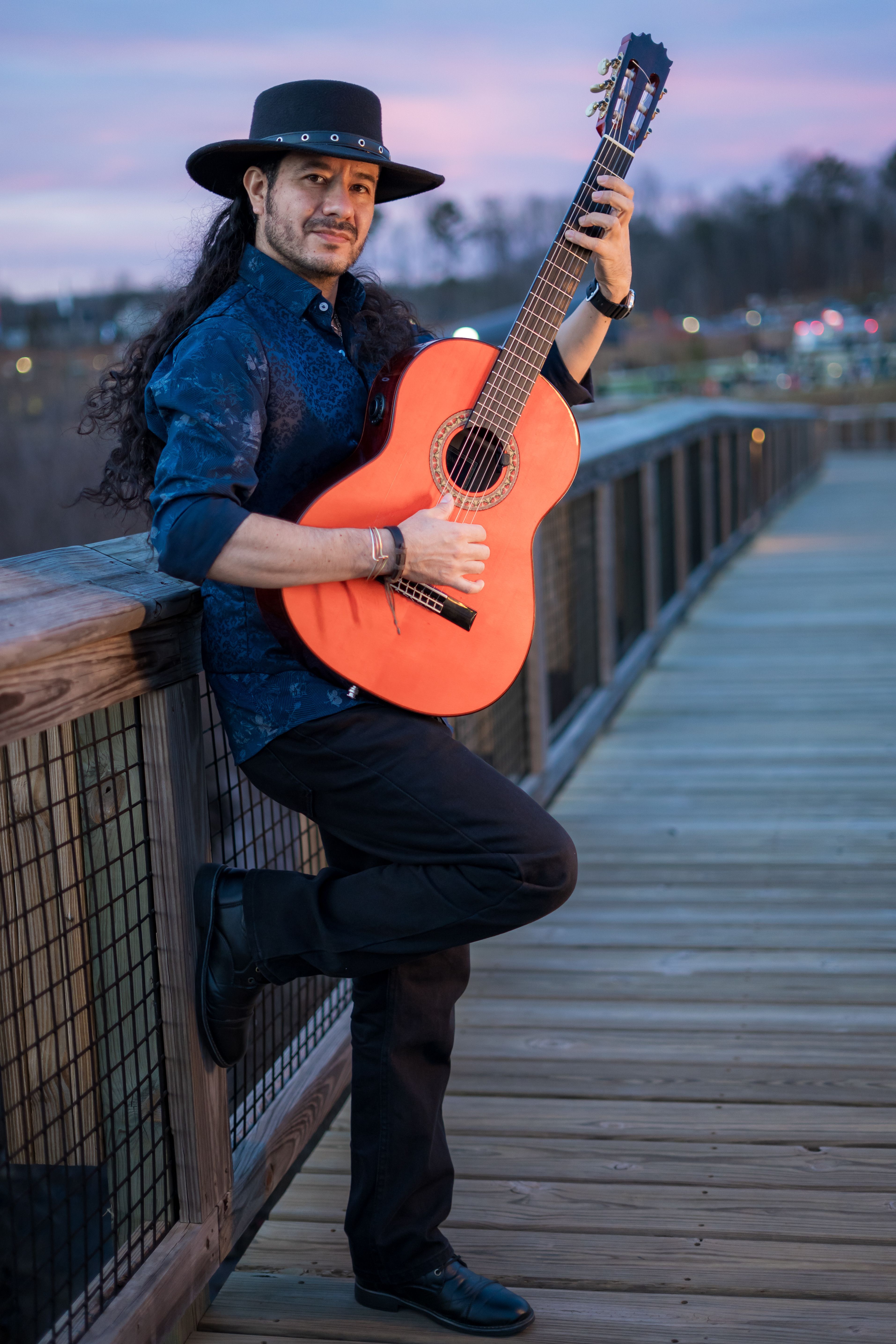 Musician with guitar on boardwalk at sunset, wearing a cowboy hat. Vibrant and artistic scene.
