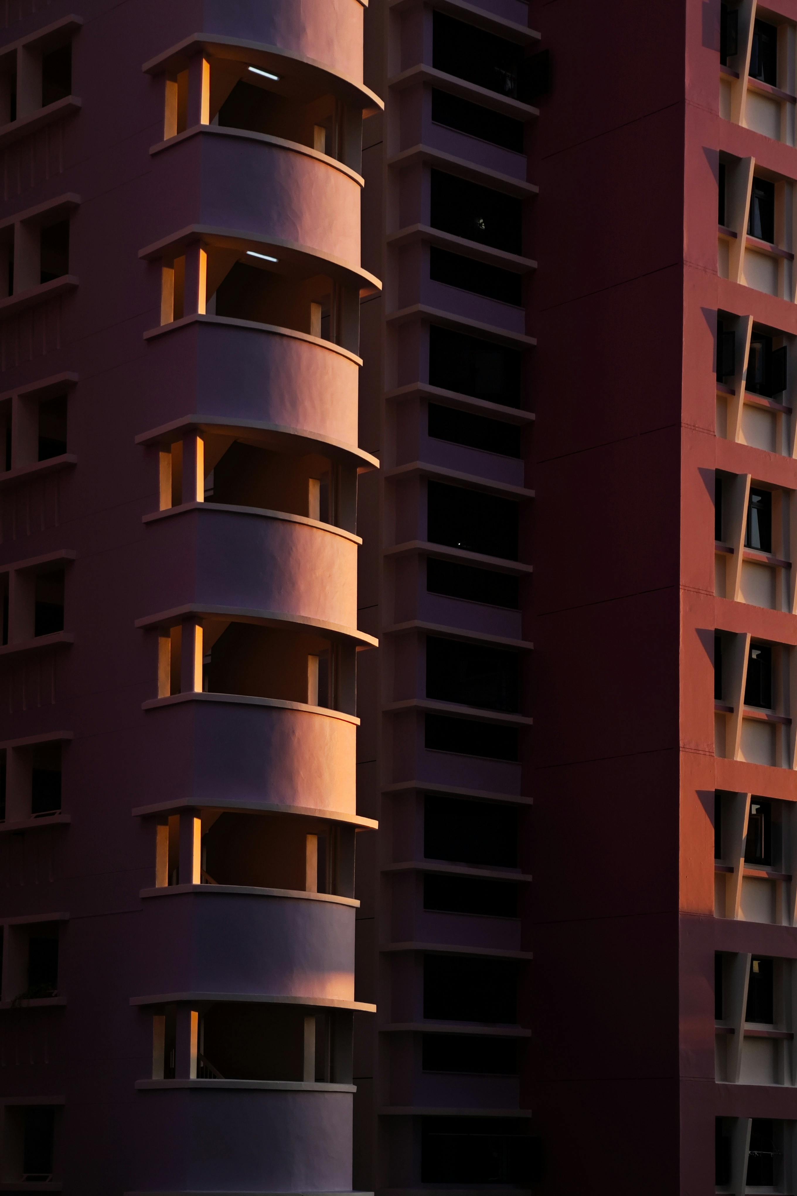 Tall modern building facade illuminated by sunset light, showcasing architectural details and shadows.