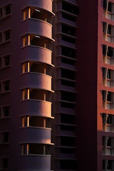 Tall modern building facade illuminated by sunset light, showcasing architectural details and shadows.