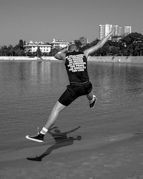 黑白照片中，一名男子在伊斯坦布尔海滨跳跃，背景是城市天际线