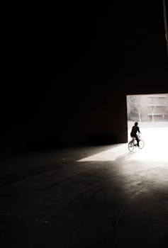 Dramatic silhouette of a cyclist emerging from a dark tunnel into bright sunlight.