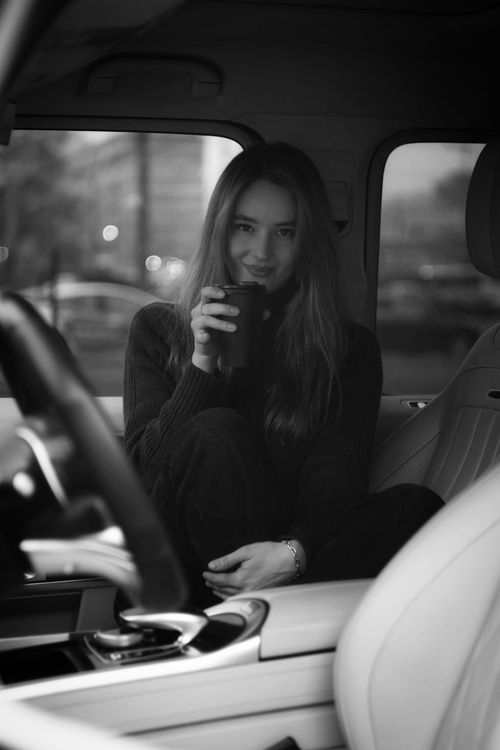 Free Portrait of a woman enjoying a coffee while sitting inside a car, captured in black and white. Stock Photo