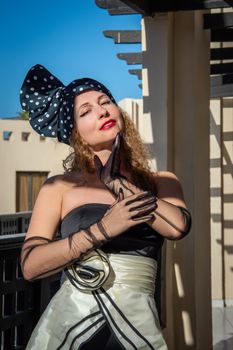 Stylish woman posing outdoors in elegant clothing and accessories under bright sunlight.