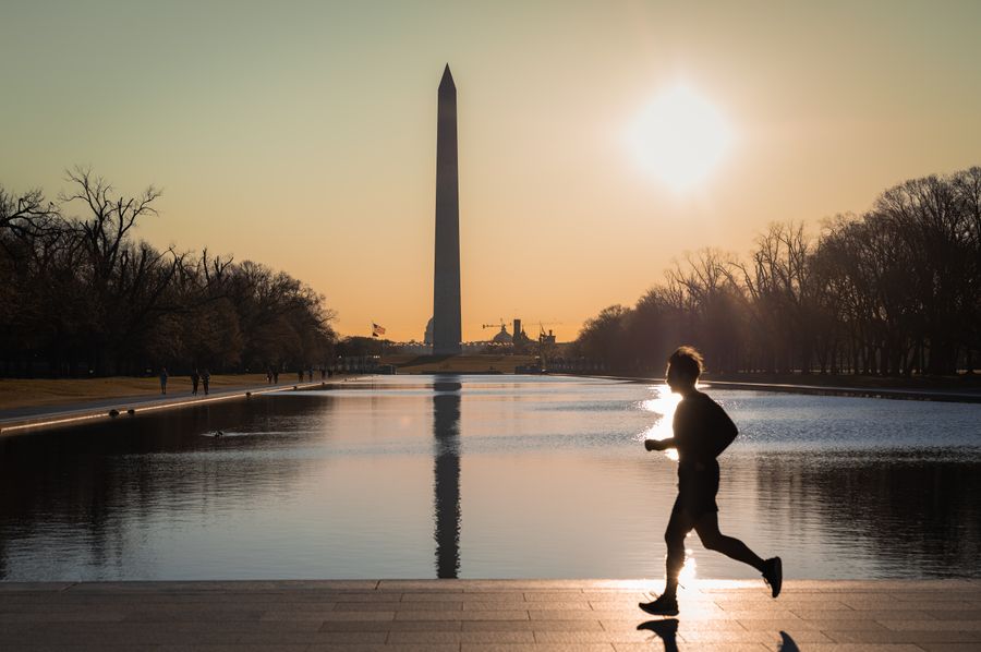 A runner silhouetted beside the Lincoln Memorial Reflecting Pool at sunrise, the Washington Monument ahead