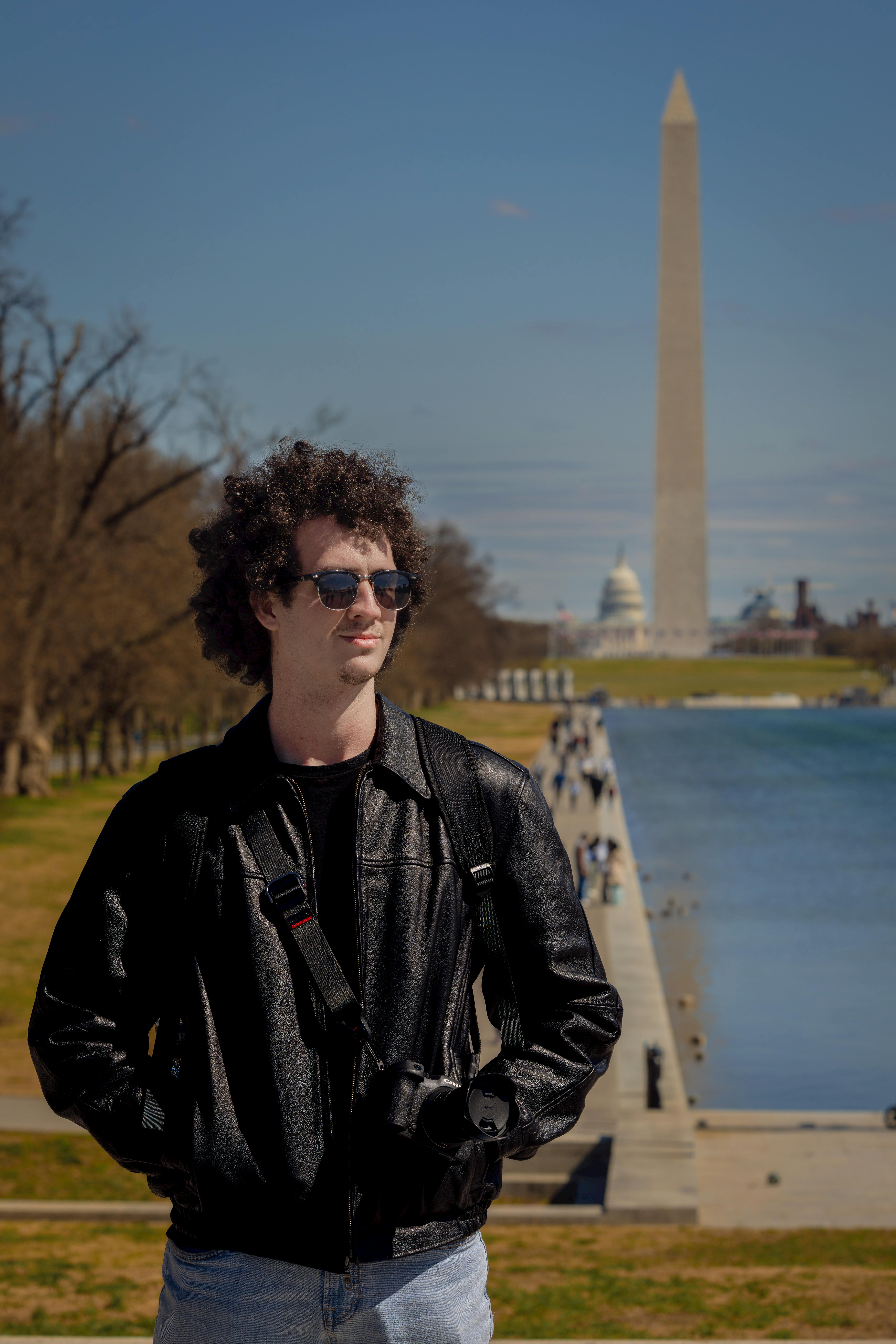 Man in a leather jacket stands by the Reflecting Pool with Washington Monument in the background.