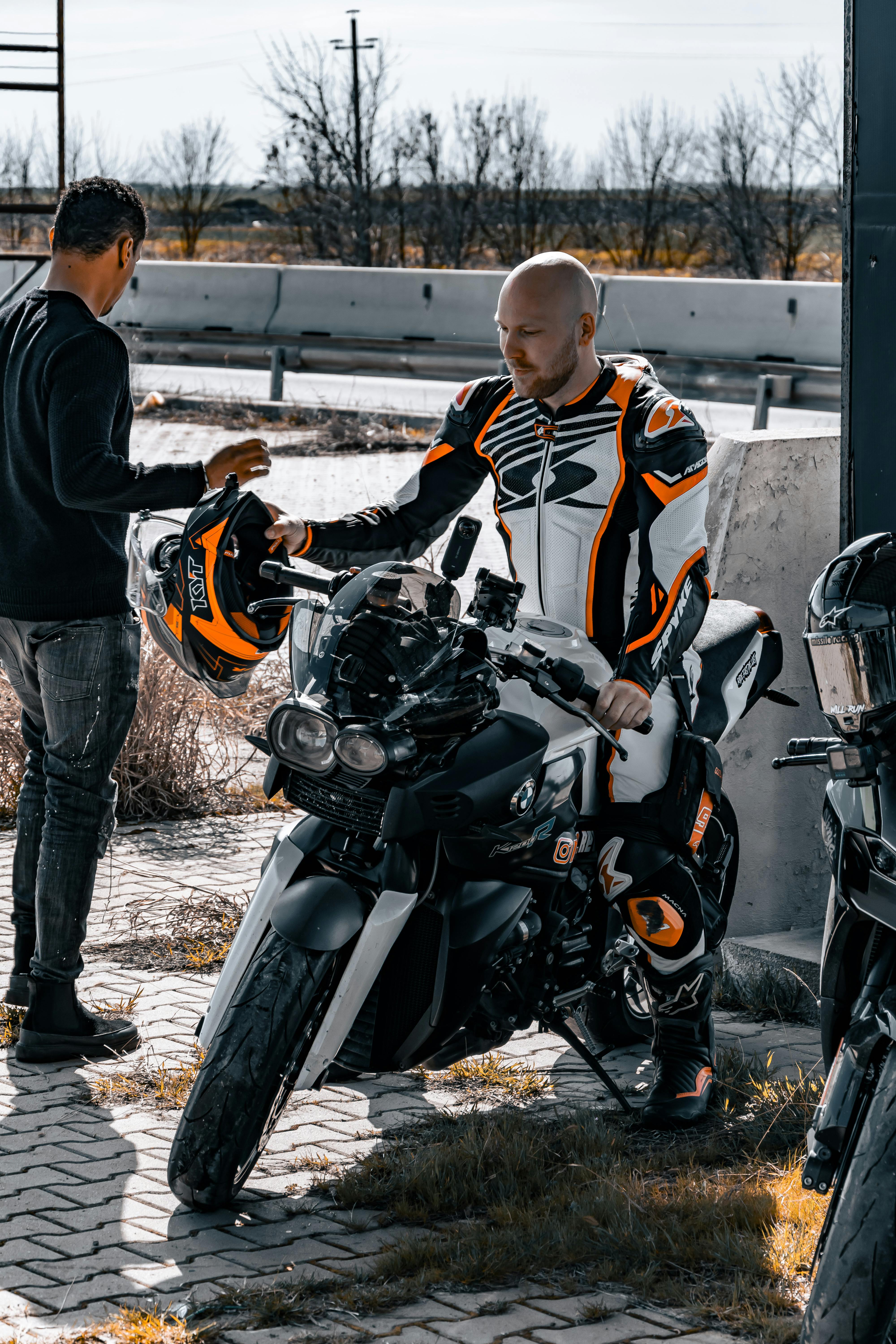 Two motorcyclists in gear prepare for a ride on a sunny day.