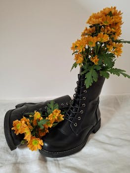 Black combat boots creatively adorned with vibrant orange flowers, exuding a unique blend of nature and fashion.