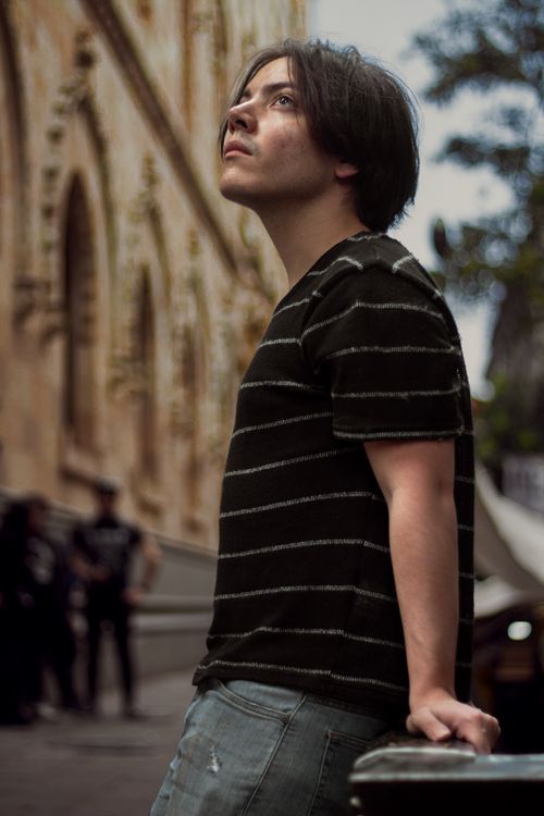 Free Pensive young man in a black shirt gazing upward near a historic building outdoors. Stock Photo