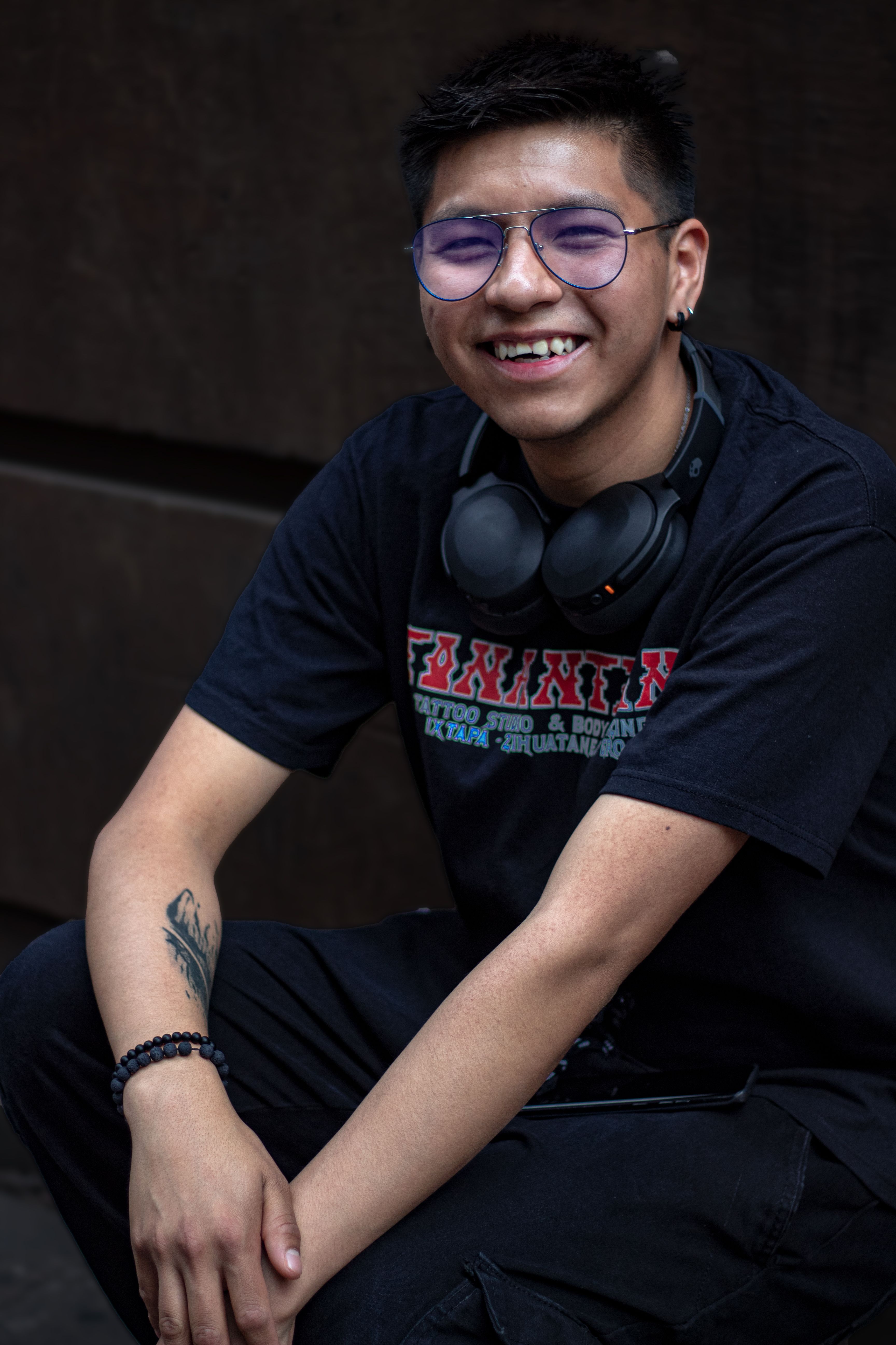 Casual young adult with headphones relaxing outside, wearing glasses and smiling.
