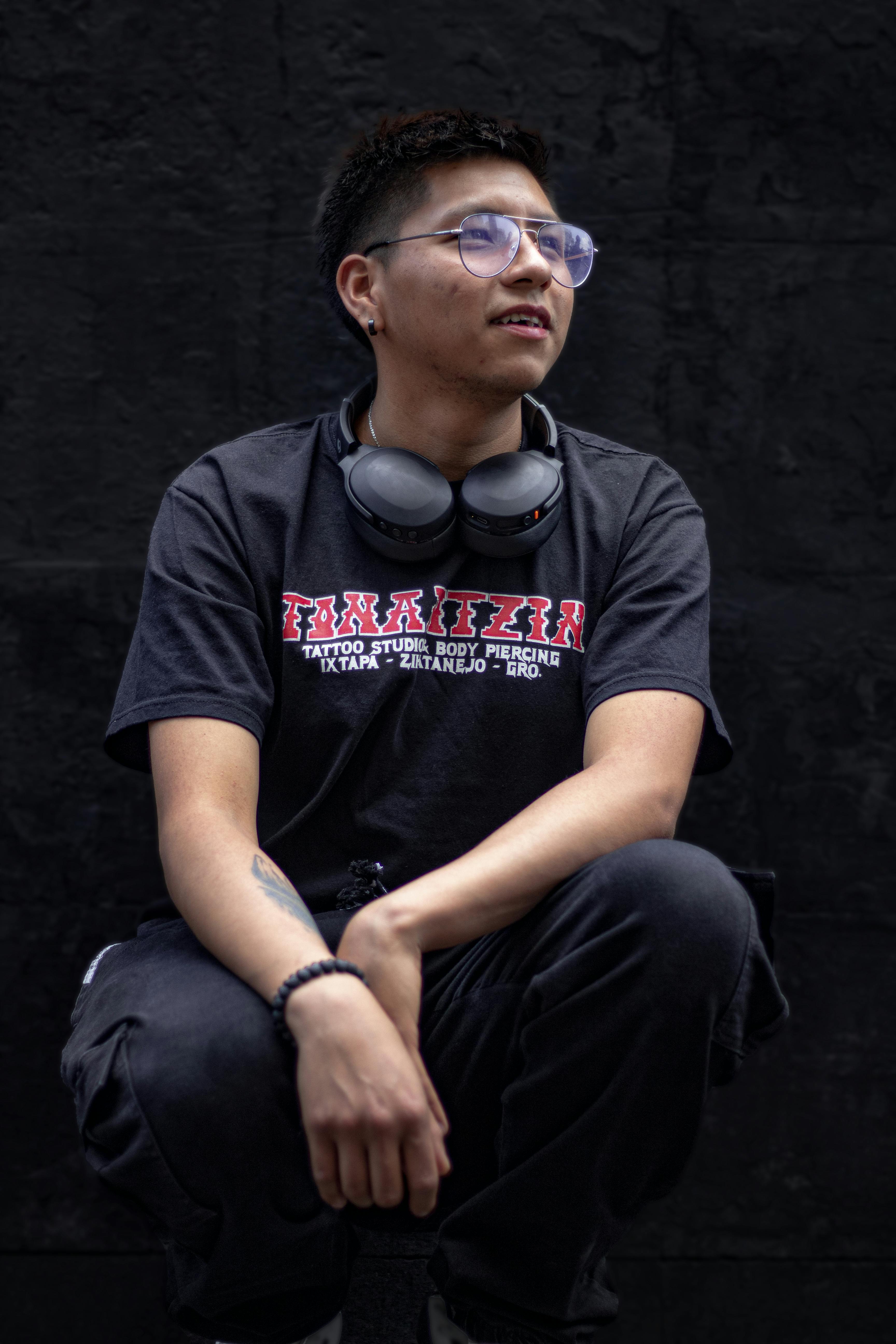 Casual portrait of a young man with headphones, sitting confidently against a dark backdrop.