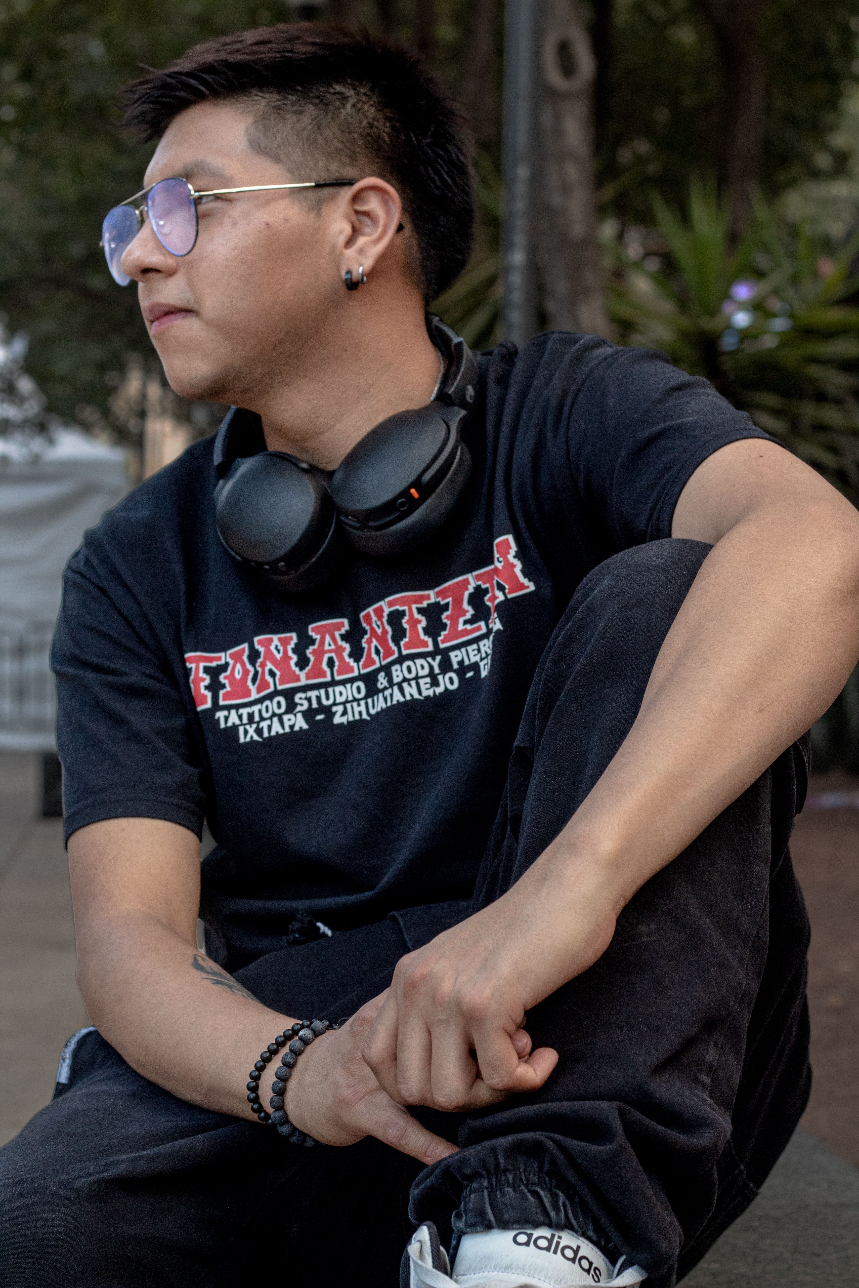 Young man in a black T-shirt sitting outdoors with headphones around his neck.